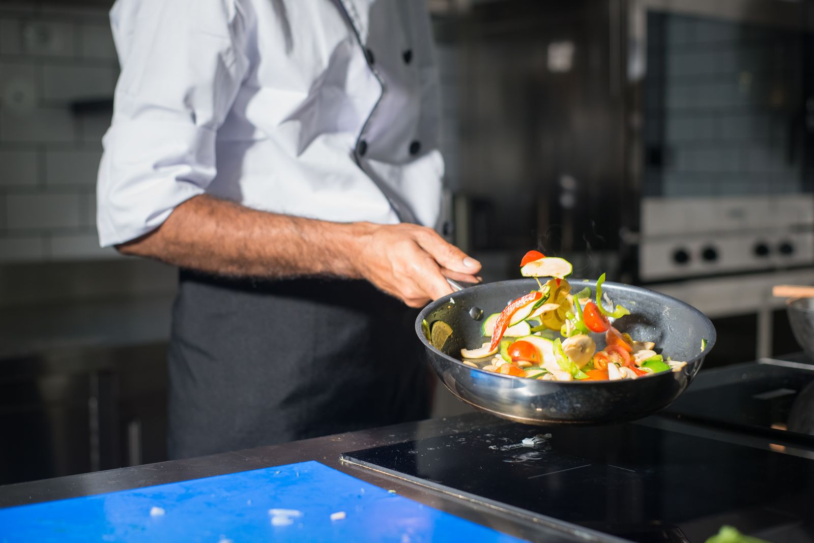 Pessoa movimentando legumes em uma frigideira na cozinha.