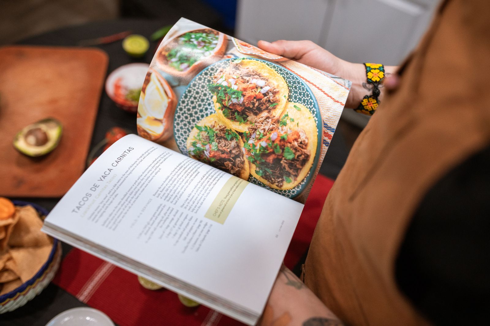 Mãos segurando um livro aberto numa página de receita com fotografia de comida.